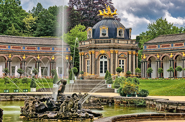 Wasserspiel eines historischen Brunnens vor romatischem mit Gold geschmückten Gebäude