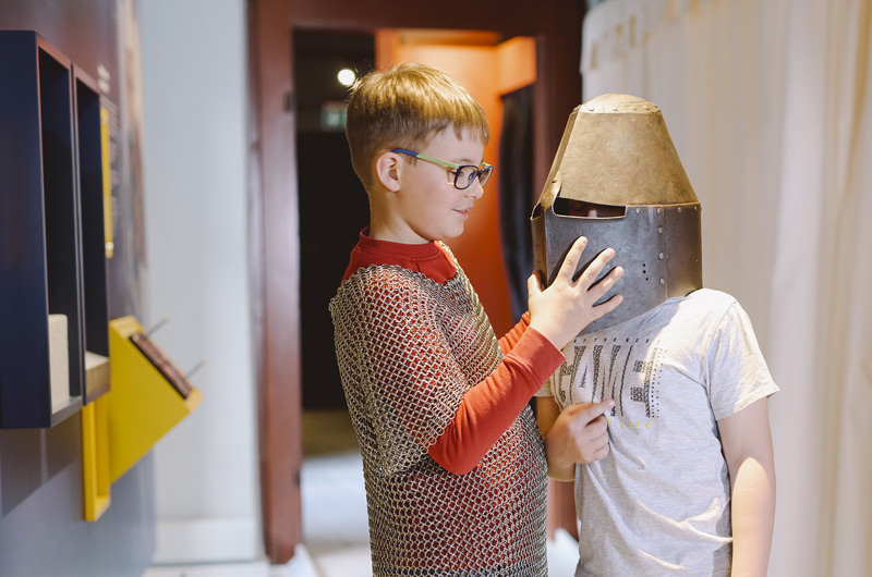 Zwei Kinder probieren Kettenhemd und Ritterhelm an