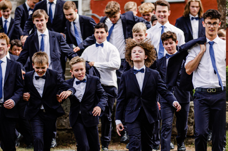 Knaben in dunkelblauen Anzügen mit Fliege laufen auf die Kamera zu