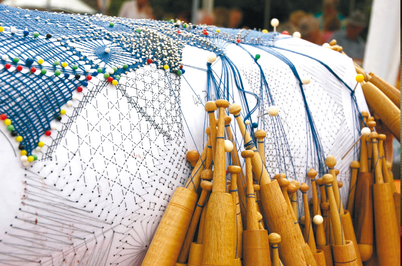 Mehrere Fäden an Klöppeln sind mit Nadeln auf einem Klöppelbrief gesichert