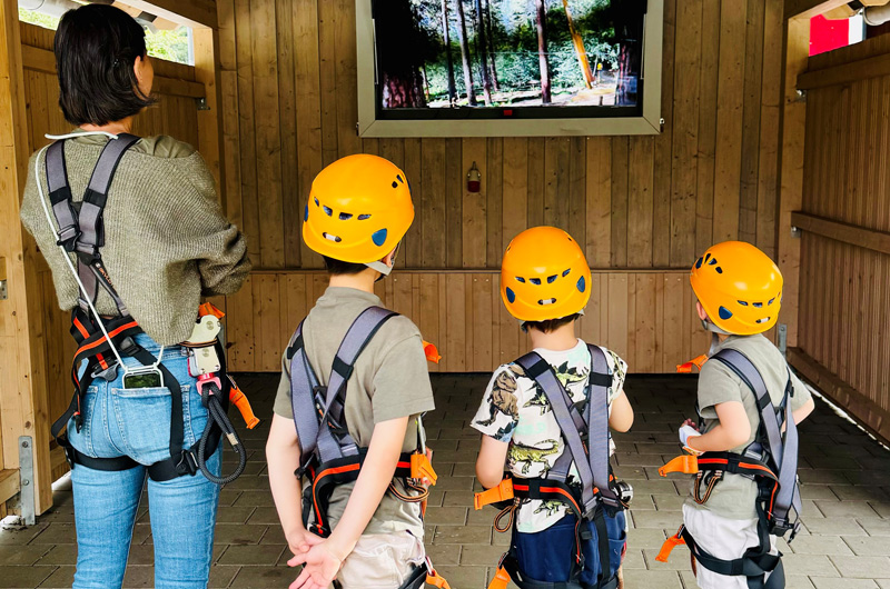 Ein Erwachsener und drei Kinder mit gelben Helm sehen sich das Einweisungsvideo im Abenteuerwald an