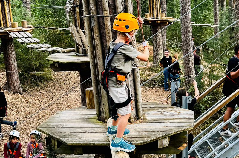 Ein Kind mit gelbem Helm und Sicherungsgeschirr klettert im Park