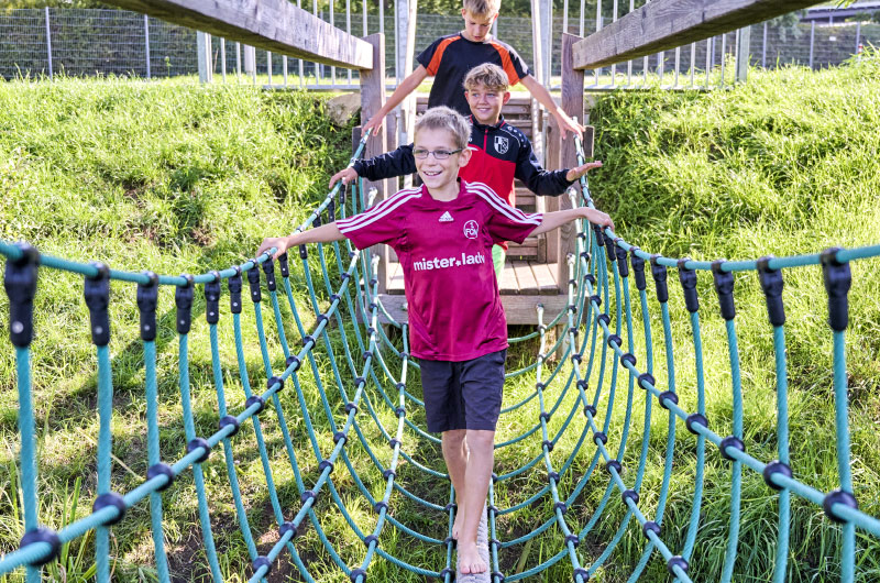 Mehrere Kinder laufen über eine Hängebrücke aus Seilen