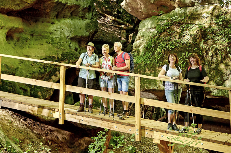 Wanderer stehen auf einer kleinen Holzbrücke vor moosbewachsenen Felsen